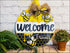 Hand painted round door hanger featuring a charming bee themed welcome sign
