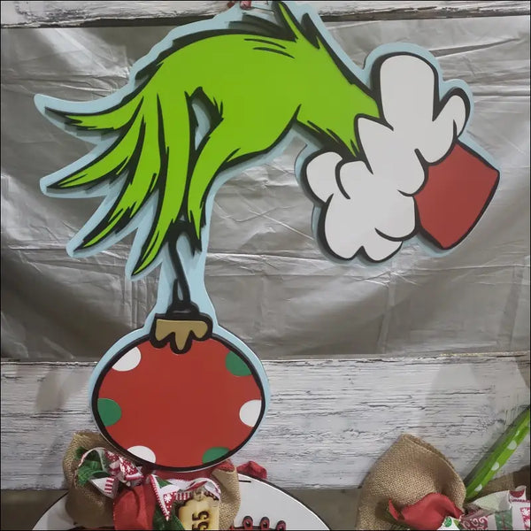 Grinch hand holding Christmas ornament on Wooden Grinch Sign for holiday door decor